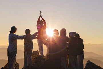 Silhouette family hands praying and holding Christian cross for worshipping God on mountain at sunrise background. Christian, Christianity, Religion copy space background. Easter Sunday concept: