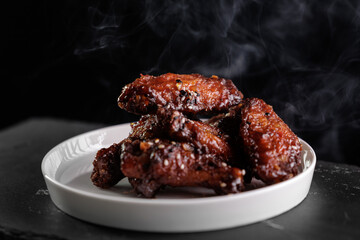 Spicy glazed chicken wings on white plate with smoky background