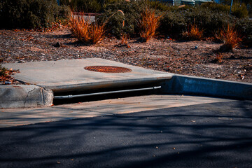 Concrete storm drain with rusty grate and metal pipe leading to underground system
