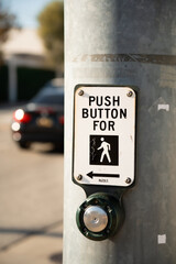 Push button for pedestrian crossing on a metal pole with a car in the background