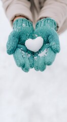 Hands holding snow heart in warm teal gloves