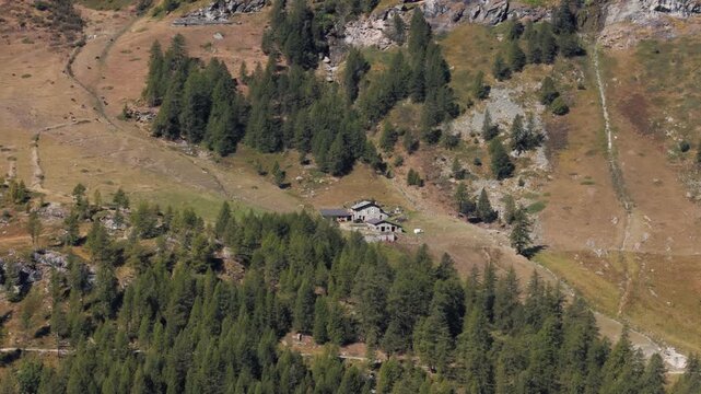 Aerial panning right of an isolated rock cabin in a mountain pine forest in Italy, Aosta Valley, Valle d&rsquo;Aosta, surrounded by alpine nature