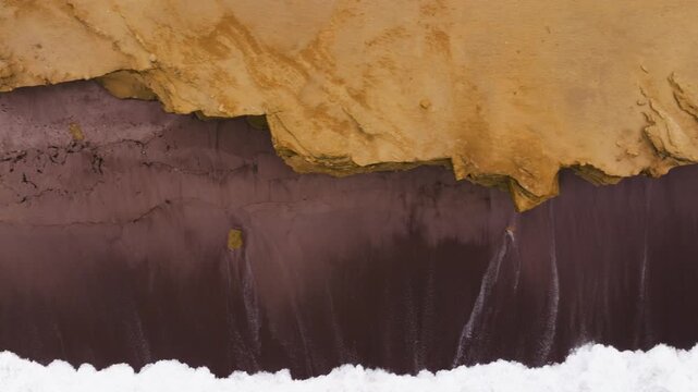 High angle tracking left across layered red cliffs dropping to surf as Paracas currents churn below, crashing waves