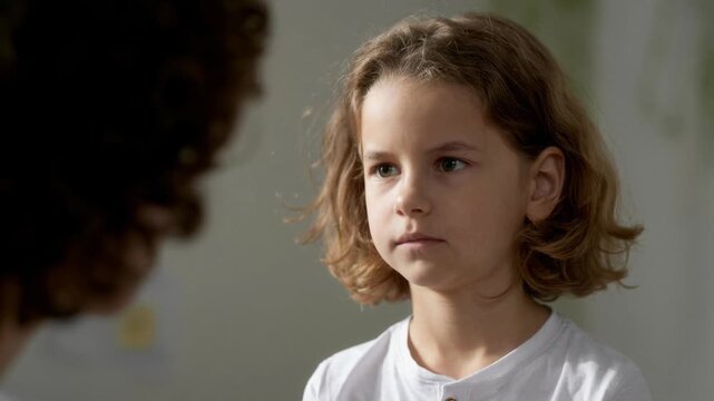 Close up on serious boy child with curly hair having conversation with parent about misbehavior in kids bedroom, AI generated footage