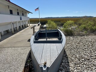 Gray boat on oyster shells next to white building overlooking marsh