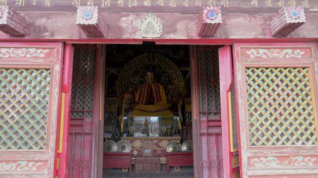 View through ornate red lattice doors at Erdene Zuu Monastery, Mongolia: a gilded Buddha statue is enshrined within a historic pavilion featuring ancient sacred altar artifacts and religious art.