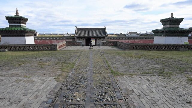 Historic entrance to Erdene Zuu Monastery in Kharkhorin, Mongolia. Wide shot of the main gate, paved stone path, and traditional stupa towers under a blue sky.