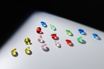 Colorful diamonds gemstones in sunlight: red, blue, green, yellow, pink gems on white surface