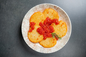 Golden potato pancakes elegantly served with bright red caviar and a sprig of dill