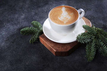 Coffee with milk in a large white cup. Drawing on the surface of a coffee drink. Fir branches and a cup of coffee on the table.