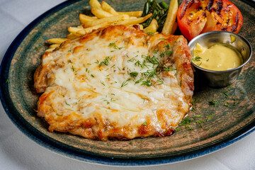 Mouthwatering chicken topped with melted cheese, served with fries and grilled tomatoes on a plate