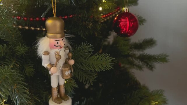 Large tin nutcracker soldier on a Christmas tree. Seasonal toy figure before an illuminated artificial Christmas tree with lights and colorful decorations. 