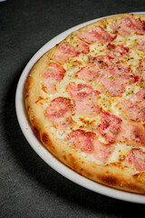A hot, fresh pizza with ham and melted cheese awaits on a dark countertop