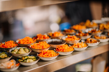 Colorful assortment of fresh vegetables in small bowls arranged on a shelf, showcasing vibrant textures and culinary presentation in a bustling kitchen environment