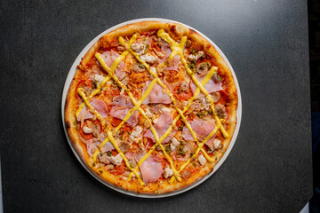 A round pizza sits on a dark table, adorned with meats and a vibrant yellow sauce pattern