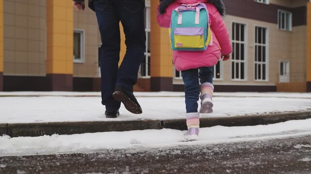 legs close-up, walking snow, child his father walk with their feet snow school building, child school backpack holds his father hand, little student goes class, parental support hand, cold snowy road