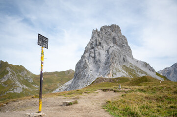 Wanderweg in den Alpen mit historischem Grenzschild vor markantem Felsgipfel in &Ouml;sterreich
