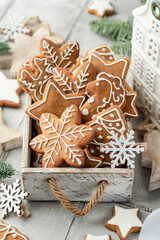 Christmas gingerbread cookies decorated with white icing in rustic wooden box. Festive holiday treats with pine branches and Christmas decor on white table