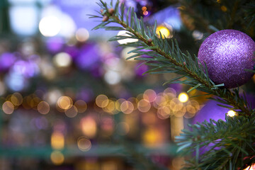 A purple ball is hanging on the Christmas tree. Christmas tree decoration. The street is out of focus. Garland with lights on Christmas tree. Place for advertis