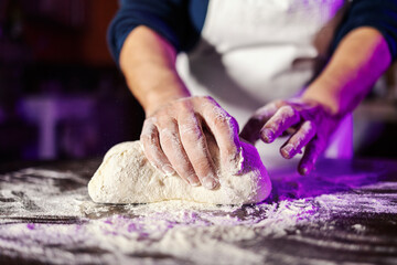Hands kneading dough with flour on dark surface