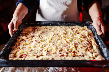 Hands holding baking tray with homemade pizza preparation