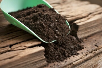 Scoop of rich dark soil spilling onto weathered wooden planks
