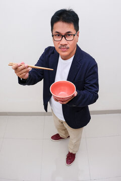 Top view of a man standing and holding red bowl and chopsticks in both hands