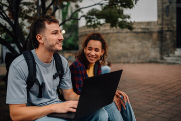 Students sharing laptop and smiling outdoors in university campus