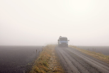 Car driving in mist on gravel road by fields in the countryside