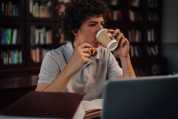 Student drinking coffee and eating pastry while studying in library