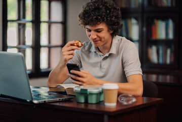 Young man working from home eating and using smartphone