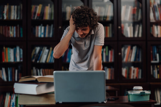 Stressed student touching head while studying on laptop in library