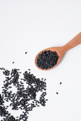 Black sesame seeds in wooden spoon isolated on white background