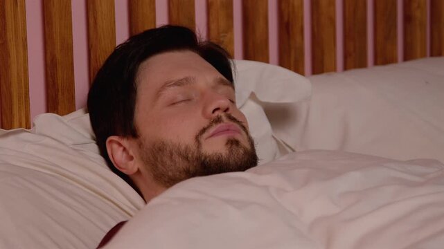 Portrait of relaxed handsome bearded middle aged man suffering from obstructive sleep apnea, sleeping tight in bed and snoring loudly while resting in bedroom at night.