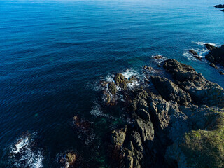 Calm waves gently lap against rugged rocks along a serene coastline under a bright blue sky at midday