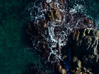 Waves crashing against rugged rocks at the shoreline during a sunny afternoon by the ocean