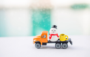 Cute snowman and coffee mug on orange truck over blurred background, Christmas card background idea