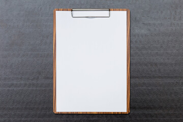 White paper on wooden clipboard on black paper background, report and check list concept, stationary and business background idea
