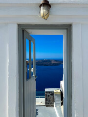 Stunning view from a door overlooking the Aegean Sea on a sunny day in Santorini, Greece with blue skies and distant islands in sight