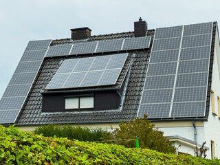 Solar panels cover a modern house rooftop, showcasing renewable energy in a quiet neighborhood setting during a cloudy afternoon