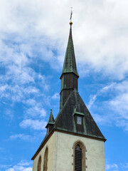 Stunning tall church steeple reaching into the blue sky against a backdrop of soft white clouds, capturing a moment of serene faith and architecture during daylight