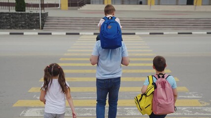 Family crossing the road to school, Children with backpacks walk with their father, The family follows the traffic rules, Morning on a school day, A safe journey to school, Dad carrying his son on his