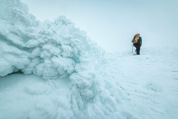 Hiker walks past ice formation in extreme alpine winter conditions