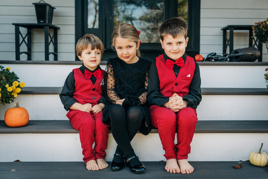 Three children dressed formally sit on porch steps in autumn