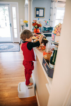 Toddler boy getting food from party buffet with stepping stool