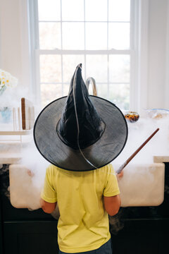 Child wearing witch hat casting magic spell in kitchen