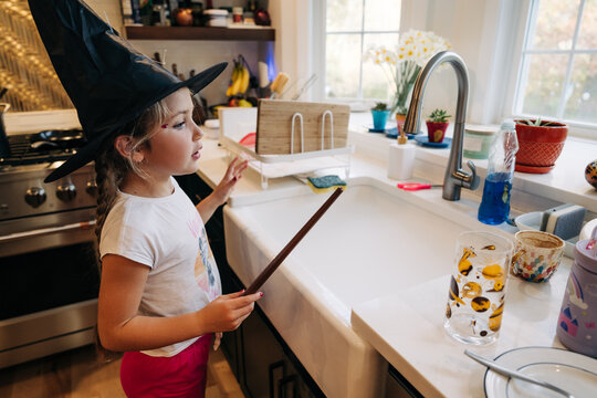 Young girl playing witch in kitchen with wand