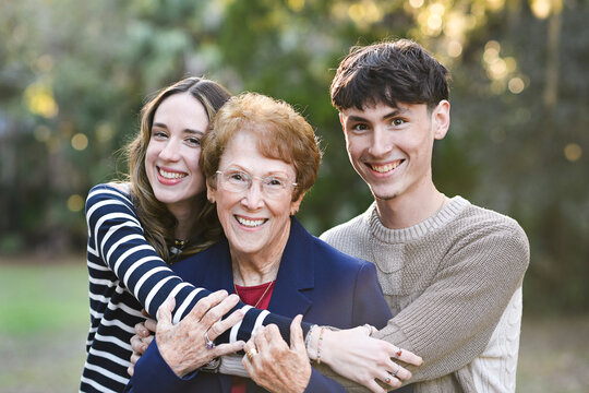 Happy grandmother hugged by two smiling young adults outdoors.