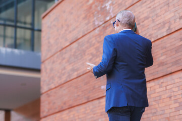 Senior businessman communicating on smartphone against modern brick wall