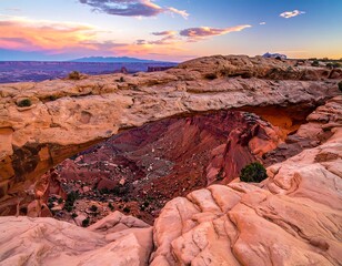 A scenic vista showcasing a natural rock arch formation with vast canyon lands and mountains under a colorful sunset